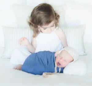 A little girl sitting on the bed with her baby brother.